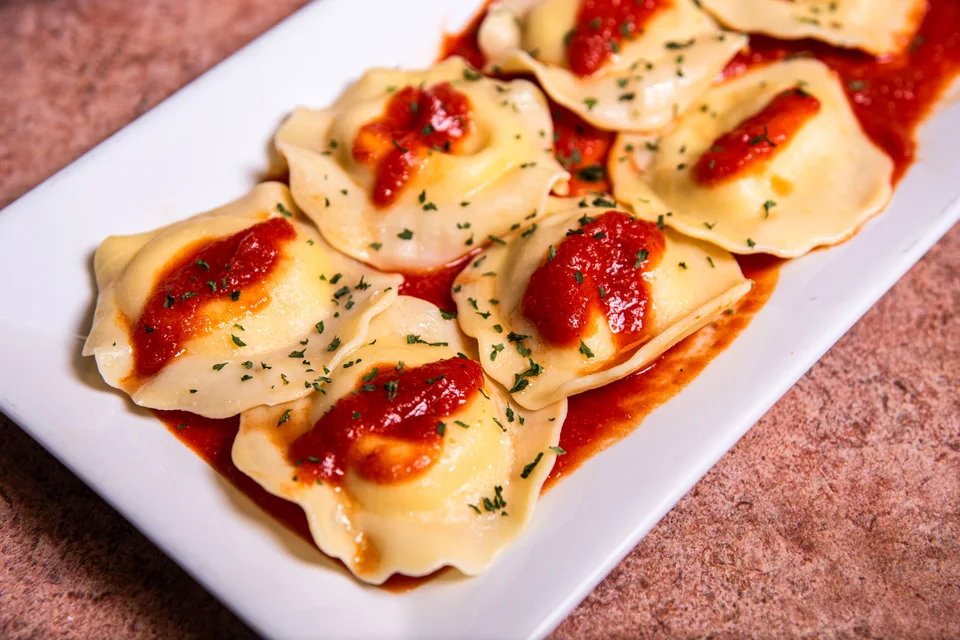 BookNoFees: Photo d’illustration : Raviolis nappés de sauce tomate et d'herbes aromatiques, présentés dans une assiette blanche