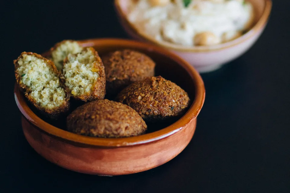 BookNoFees: Photo d’illustration : Boulettes de falafel, dont une coupée en deux, dans un bol avec du houmous à l'arrière-plan