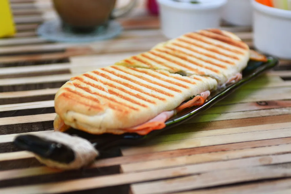 BookNoFees: Photo d’illustration : Un panini grillé présentant des marques de grillade, servi sur une assiette foncée