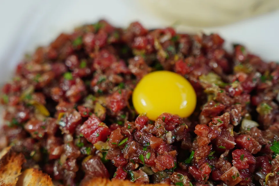 BookNoFees: Photo d’illustration : Steak tartare garni d'un jaune d'œuf et servi avec du pain grillé
